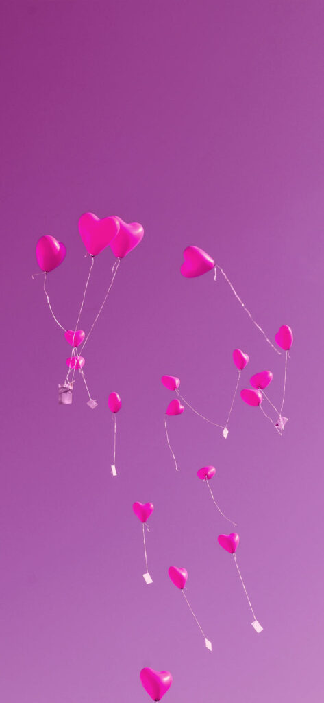 A group of pink heart-shaped balloons with attached notes, floating against a purple background. Free Valentines Aesthetic Wallpapers