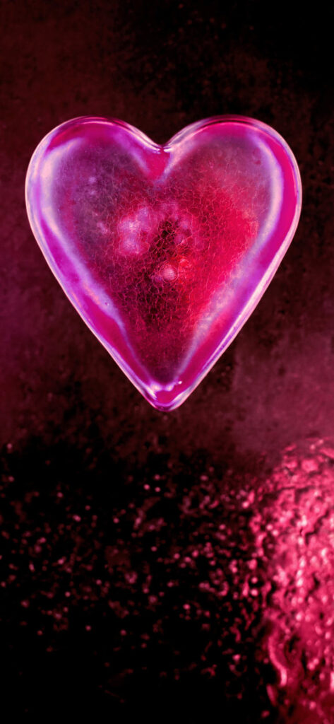 A glowing heart-shaped object illuminated in pink and purple hues, floating against a dark, textured background with similar color tones.