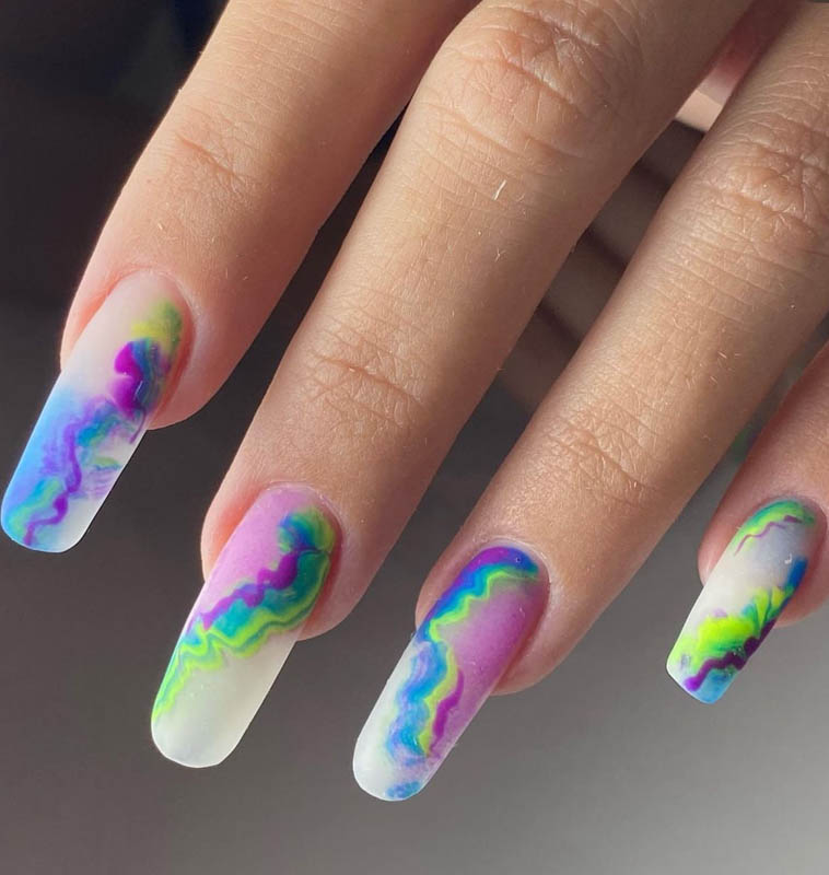 A close-up image of a hand displaying nails with a colorful, marbled design incorporating shades of green, blue, purple, and white.
Spring Nail Ideas For 2024.