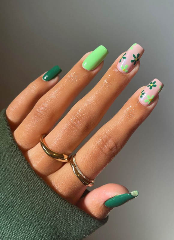 A hand with green and pink floral nails and gold rings.