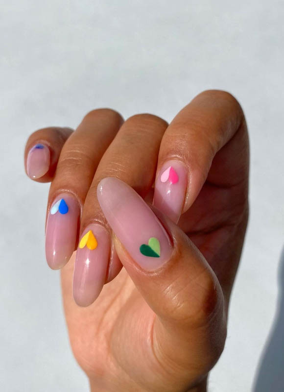 A hand with pink nails and colorful hearts on a white background. Spring Nail Ideas For 2024.