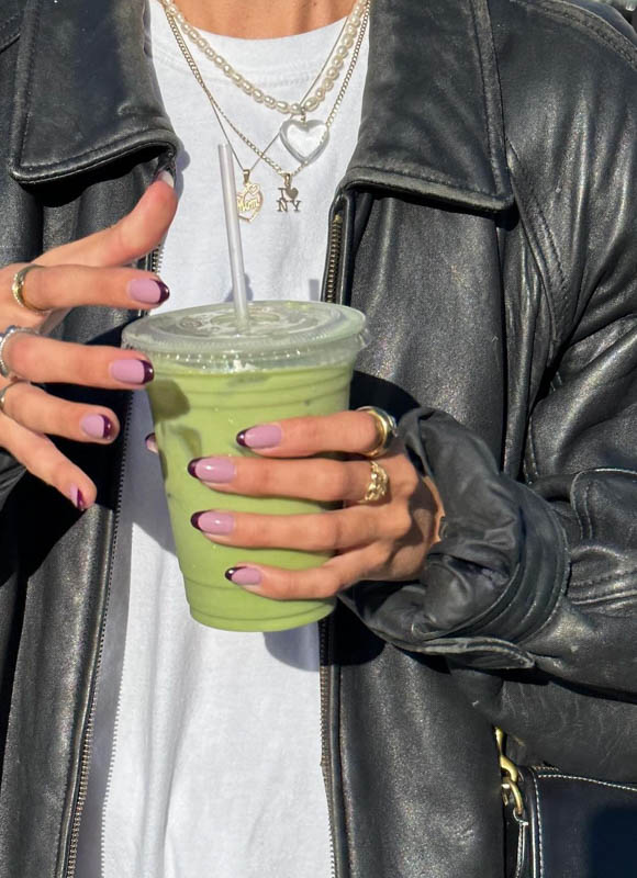 A person holding a green smoothie and wearing a leather jacket and necklaces. Spring Nail Ideas For 2024.