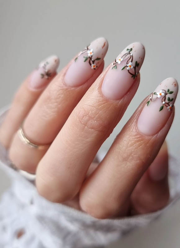 Spring Nail Designs For 2024. A close-up of a hand with nails adorned with delicate floral nail art, and a gold ring on the ring finger.

