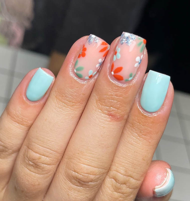 Spring Nail Designs For 2024. A hand with teal and orange floral nail art.

