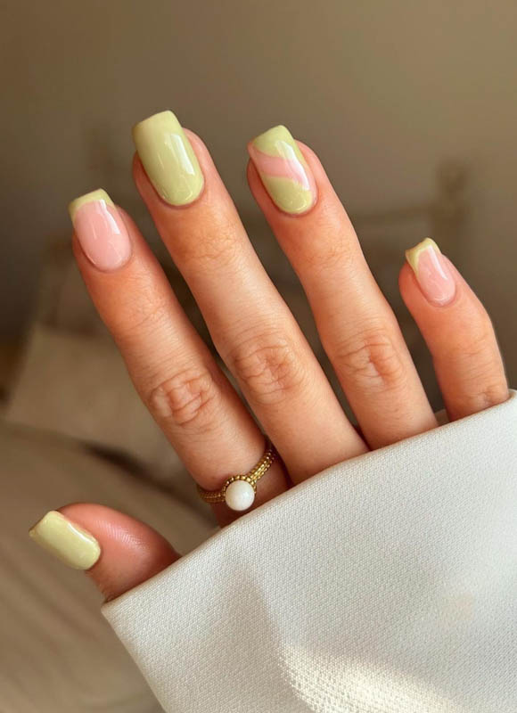 A hand with pastel pink and green nails and a pearl ring on white fabric.
Spring Nail Ideas For 2024.