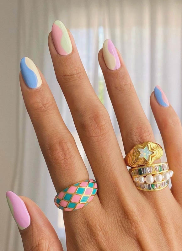 A hand with colorful pastel nails and stylish rings against a soft background. Spring Nail Ideas For 2024.