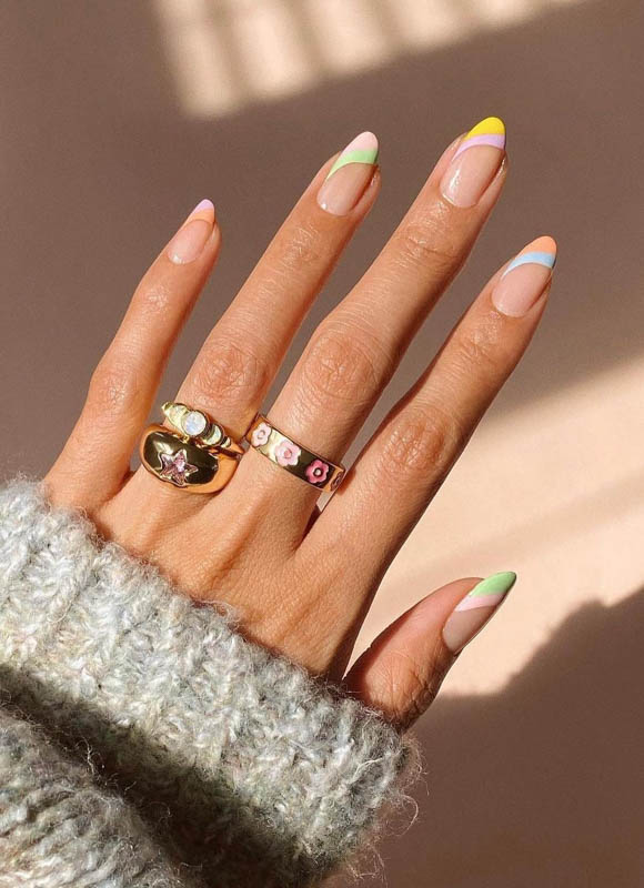 A hand adorned with colorful nail art and two elegant rings, casting a soft shadow on a surface. Spring Nail Ideas For 2024.