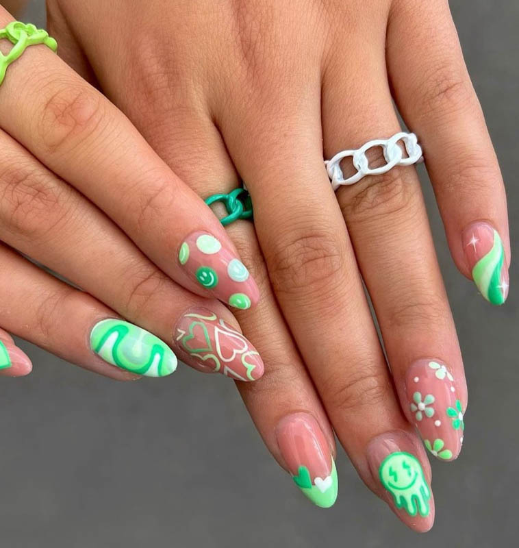 A close-up of hands with detailed mint green nail art and colorful rings.

