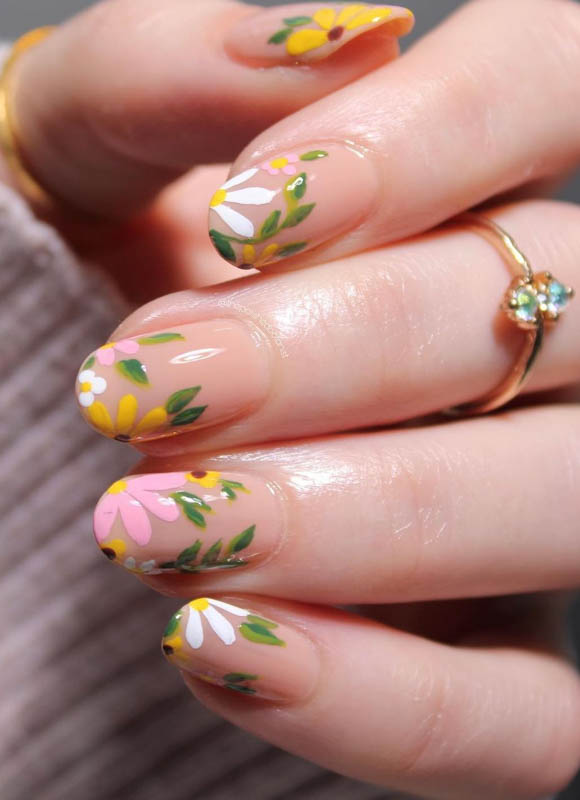 Spring Nail Designs For 2024. A close-up of a hand with floral nails and a gold ring with gemstones.

