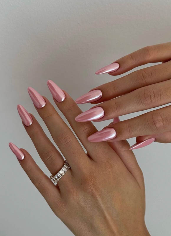 Two hands with long, glossy, pink pearl nails and a sparkling ring against a neutral background. Spring Nail Ideas For 2024.