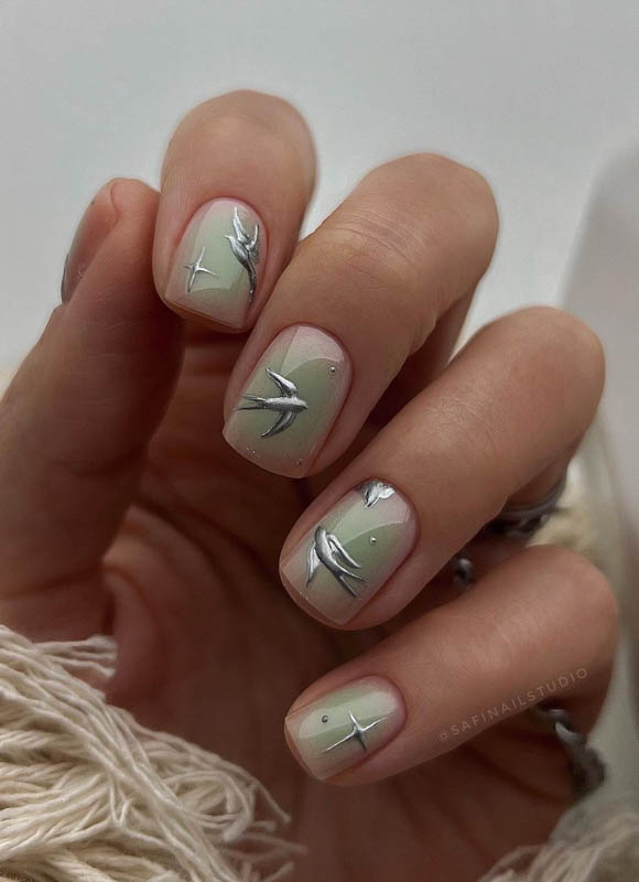 A hand with light nails and silver botanical line art, against a white background.

