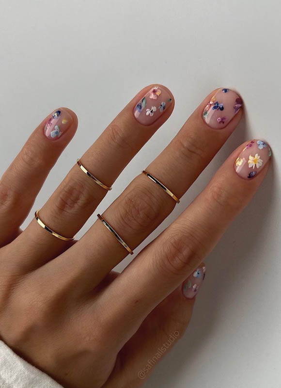 Spring Nail Designs For 2024. A hand with pastel floral nail art and delicate gold rings.

