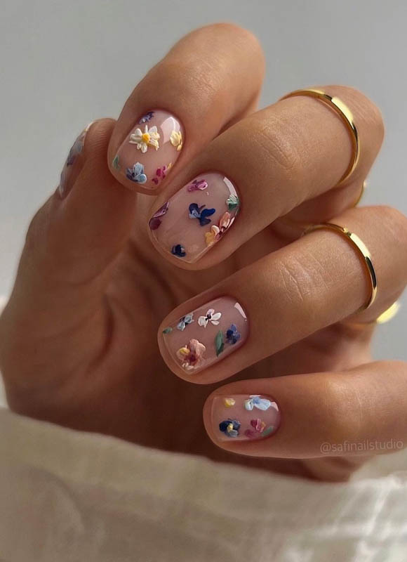 Spring Nail Designs For 2024. A hand with pastel floral nail art and delicate gold rings.

