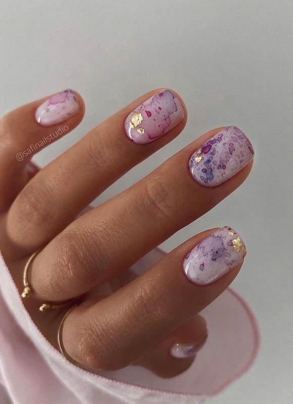 A hand with artistic nails and gold rings on a pink surface

