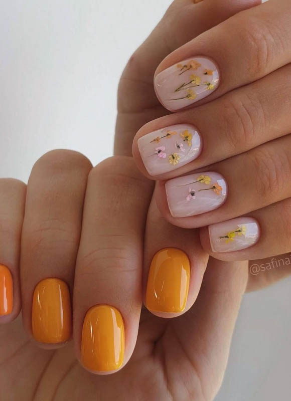 Spring Nail Designs For 2024. A close-up of two hands showcasing beautifully painted nails; one hand with pale pink nail polish adorned with delicate gold flakes and the other with glossy, vibrant orange nail polish.

