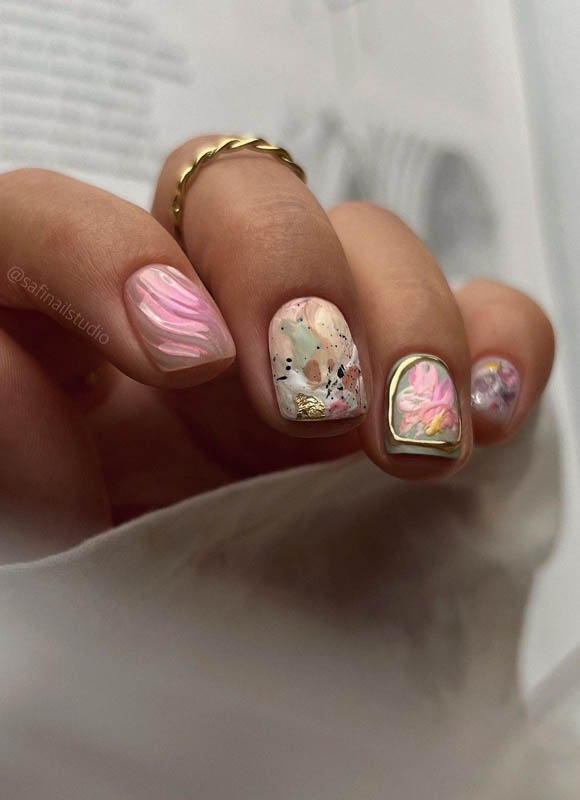 A hand with various nail art designs and a gold ring on a page of text

