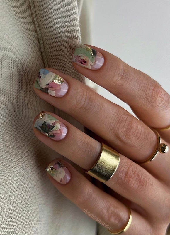 A hand with floral nail art and gold rings on a light fabric background

