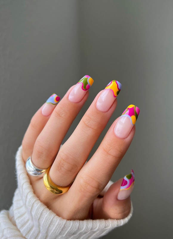 A hand with abstract nail art and rings against a grey background.

